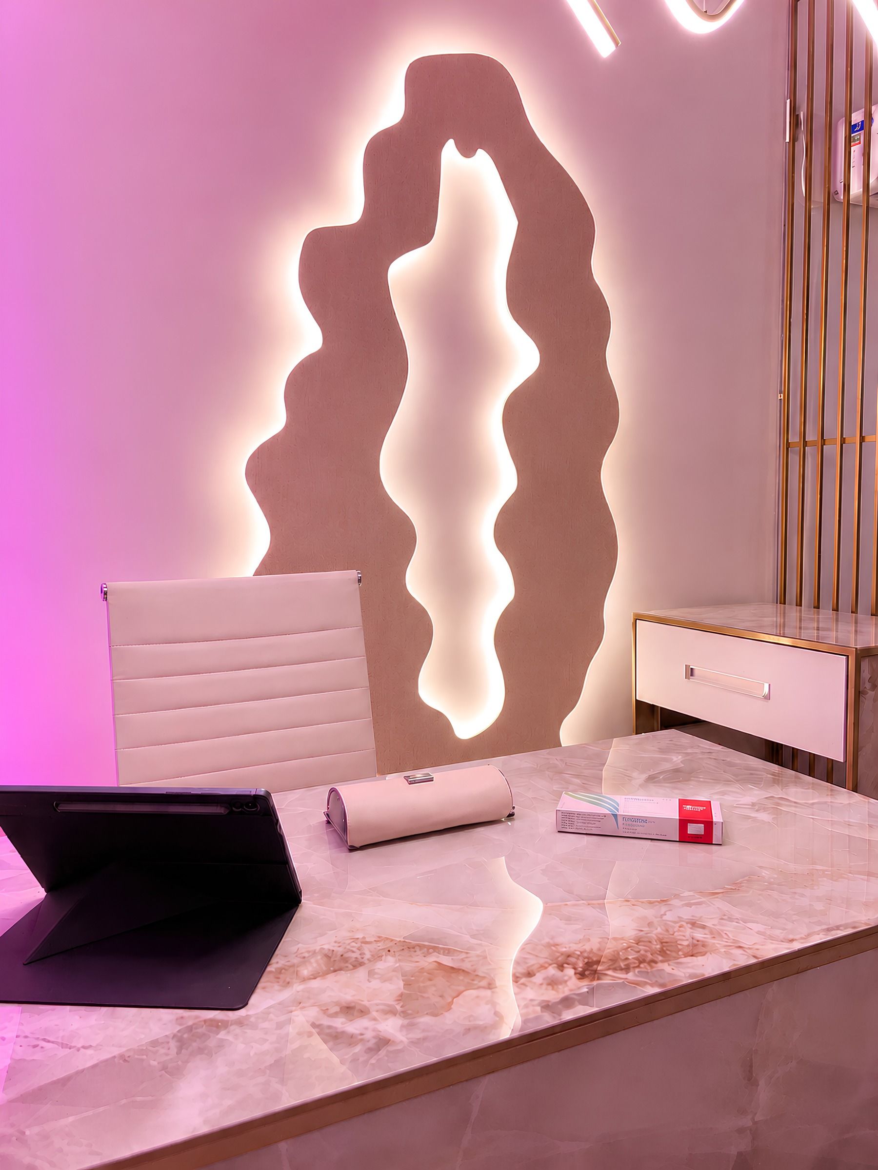 Consultório com painel de madeira ondulado iluminado por trás e luz magenta nas paredes