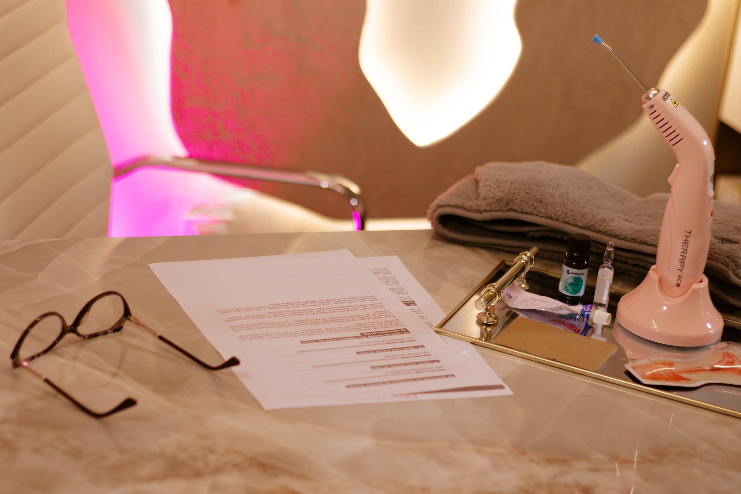 Mesa da consulta, com óculos, papéis e um modelo anatômico, diante do painel iluminado